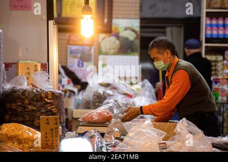 Taipei, Taiwan. 8 febbraio 2021. Un venditore di strada che indossa una maschera di vendita stagionale Lunar New Year sundries, compresi noci, frutta secca, e carne a scatti. Il mercato lunare di Capodanno di Taipei su Dihua Street sara' cancellato a causa di problemi relativi al COVID-19. Credit: SOPA Images Limited/Alamy Live News Foto Stock