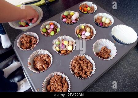 Bambini che fanno e decorano torte di riso al cioccolato con astuccie e mini uova Foto Stock