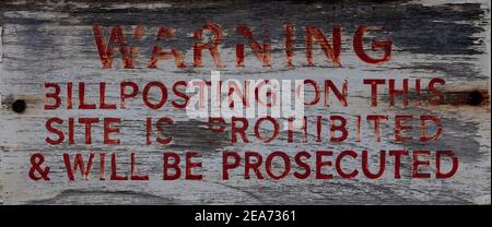 Vecchio e sbiadito segno di legno in vernice rossa a Kensington, Londra che indica che Bill Posters sarà perseguito. Foto Stock