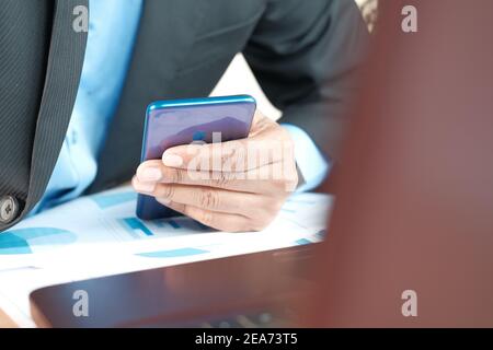 giovane uomo che lavora sulla scrivania dell'ufficio e utilizza lo smartphone Foto Stock