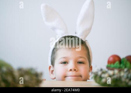 Divertirsi con la caccia all'uovo di Pasqua. Bambino che indossa orecchie conigliate e dipinge le uova. Foto Stock