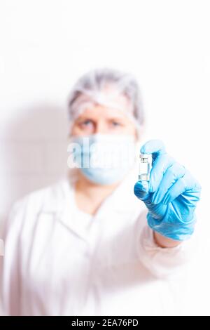 Donna medico in medicina protettiva uniforme e maschera che contiene ampolla. Arrestare il concetto di coronavirus. Mettere a fuoco sul flacone. Medico irriconoscibile e offuscato. Foto Stock