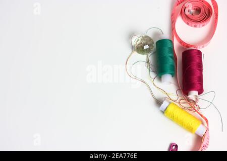 Bobine di filo multicolore, nastro di misurazione rosa e un perno rosa su una piastra bianca da tavolo. Lavoro di ago, cucito, e riparazione dei vestiti. Spazio per t Foto Stock