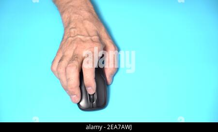 Isolato su sfondo bianco. La mano di un vecchio uomo tiene un mouse per computer wireless sul tavolo. Fare clic e spostare Foto Stock