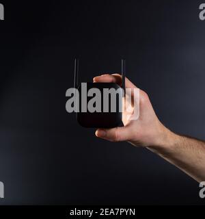 Mano che collega l'amplificatore wifi nero alla presa elettrica, su sfondo nero. Foto Stock