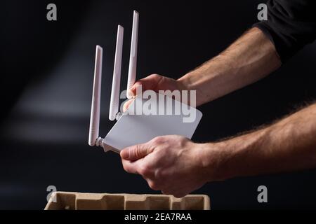 Mani dell'uomo che tengono il nuovo router wifi su sfondo nero. Disimballaggio del nuovo router bianco. Foto Stock