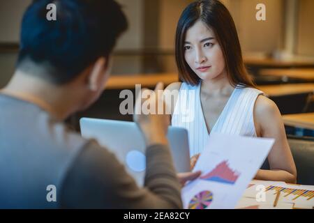 Vista posteriore di Furious boss scolding asiatica giovane donna d'affari in vestito casual da punto a faccia circa prestazioni e KPI in ufficio moderno, Business Foto Stock