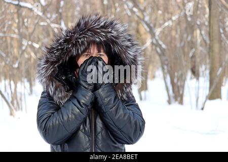 Donna surgelata in camice di pelle con cappuccio di pelliccia in piedi all'aperto con la sua mano guanto che copre il viso. Ragazza cercando di mantenere caldo, il concetto di clima freddo Foto Stock