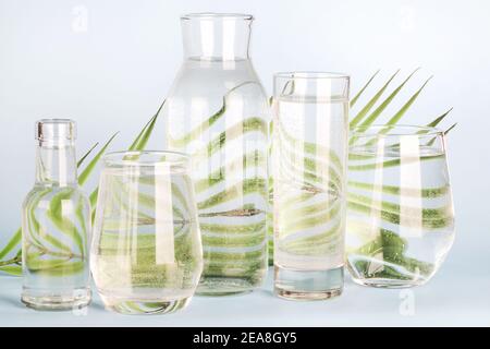 foglia di palma distorta attraverso l'acqua in bicchieri e bottiglie su sfondo blu. Arredamento domestico, eco-friendly, acqua pura, giardinaggio concept.natura sfondo Foto Stock