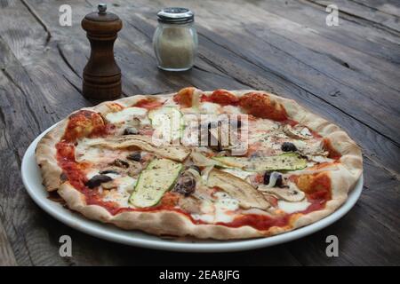 Una pizza vegetariana rustica cotta in legno con shaker di sale e pepe su un tavolo di legno. Foto Stock