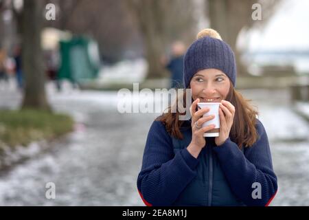 Donna bruna felice di mezza età che va per una passeggiata e bere un caffè da andare Foto Stock