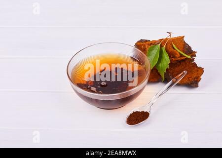 Pezzi di funghi Chaga, cucchiaio trasparente con polvere, tazza da tè in vetro isolata su sfondo bianco, primo piano. Foto Stock