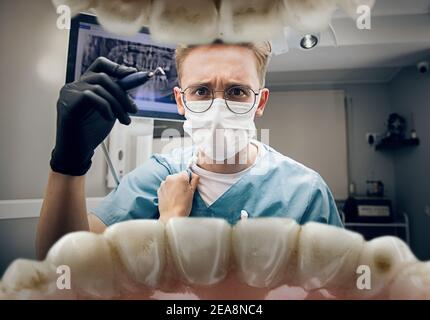 Le mani femminili si staccano dall'accappatoio. Medico che guarda in bocca, controllo, esame dei denti. Utilizzo di attrezzi e attrezzature. Sanità e medicina, stomatologia, sentimenti di paziente. Guardare dall'interno dei denti. Foto Stock