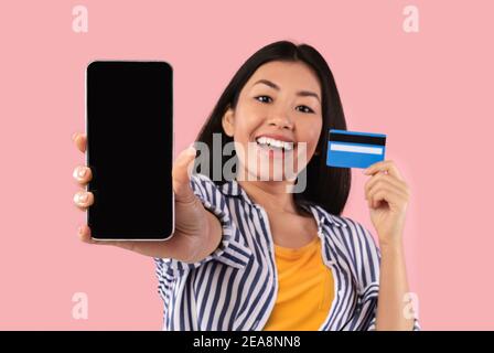 Donna asiatica che mostra lo schermo vuoto dello smartphone e la carta di credito Foto Stock
