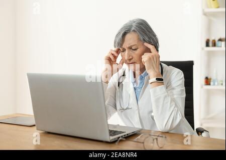 Stanco depresso medico anziano seduto da solo in ufficio di fronte a un computer portatile, sensazione di burnout al lavoro o disperato e pensare a un medico Foto Stock