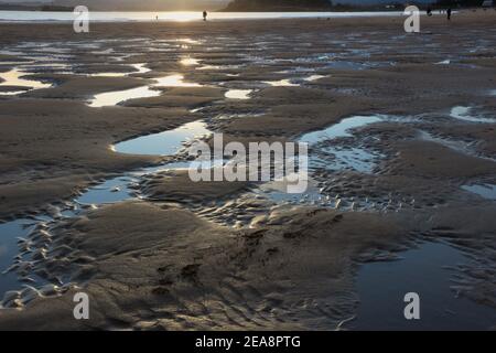 Persone in spiaggia a bassa marea con un modello di sabbia e acqua di mare con il cielo riflesso in acqua prima mattina Santander Cantabria Spagna Foto Stock