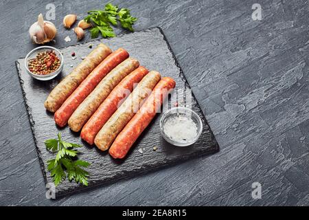 Macellai crudi salsicce su ardesia con erbe. Vista dall'alto. Foto Stock