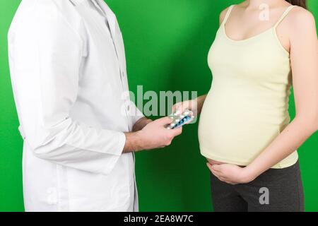 Ginecologo maschile giving pillole a donna incinta durante l'appuntamento a sfondo colorato. Visita A un medico gravidanza Sanità e persone concetto. Foto Stock