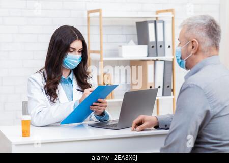 Medico in maschera medica di consultazione del viso a pazienti anziani durante covid-19 pandemia Foto Stock