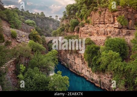 Antico ponte ad arco sulla gola del fiume Kopruray nel Parco Nazionale di Koprulu in Turchia. Vista panoramica del canyon e delle montagne dalle tempeste blu riv Foto Stock