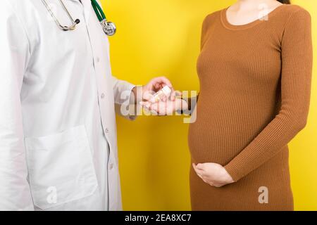 Ginecologo maschile giving pillole a donna incinta durante l'appuntamento a sfondo colorato. Visita A un medico gravidanza Sanità e persone concetto. Foto Stock