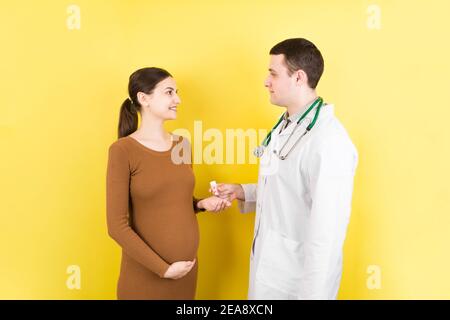 Ginecologo maschile giving pillole a donna incinta durante l'appuntamento a sfondo colorato. Visita A un medico gravidanza Sanità e persone concetto. Foto Stock