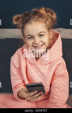 Primo piano foto di un'affascinante ragazza che sorride alla macchina fotografica mentre si tiene in mano un telefono e si sta chattando su di esso Foto Stock