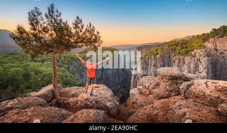 Un uomo libero a braccia aperte si trova sulla cima di una scogliera sopra la gola del canyon di Tazi in Turchia. Solitudine in natura e attivo viaggio e ricreazione Foto Stock