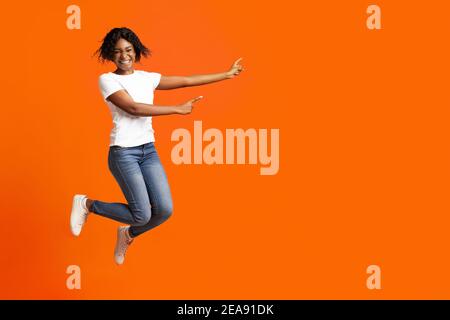Donna millennial afroamericana emozionale sorridente e indicando la pubblicità Foto Stock