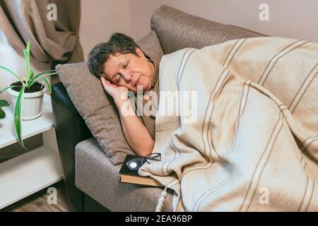 La donna anziana si sentiva addormentata mentre leggeva sul divano Foto Stock