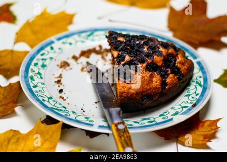 Defocalizzare un primo piano di torta al cioccolato su un piatto bianco con motivi ornati blu. Brownie. Torta. Sfondo bianco con sciarpa a scacchi. Coltello Foto Stock