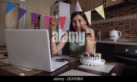 Donna che celebra il suo compleanno attraverso videochiama festa virtuale con gli amici. Si lit e soffia fuori candela. Ambiente di lavoro domestico decorato in modo autentico. Coronavir Foto Stock