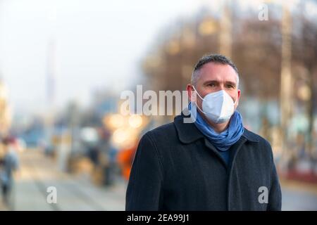 Uomo che indossa una maschera di protezione che cammina su una strada cittadina. Foto Stock