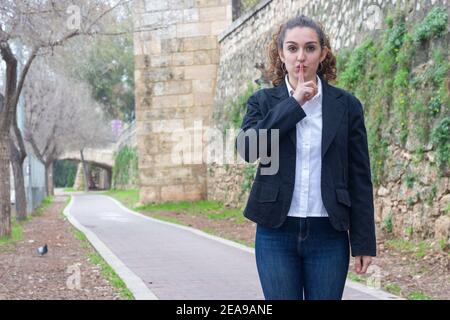 Bella donna d'affari che fa il segno 'shush' all'aperto Foto Stock