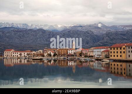 Piccola città costiera di Vinjerac in Croazia al mattino presto con mare calmo, riflessi in acqua e montagne sullo sfondo. Foto Stock