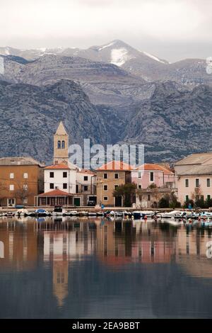 Piccola città costiera di Vinjerac in Croazia al mattino presto con mare calmo, riflessi in acqua e montagne sullo sfondo. Foto Stock