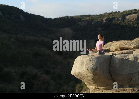 Yogi facendo yoga e meditando nella parte superiore di a. scogliera in montagna Foto Stock