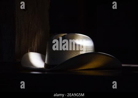 Un cappello da cowboy di paglia si trova in cima a un bar. È illuminato dalla luce naturale attraverso alcune finestre a soffitto. Foto Stock