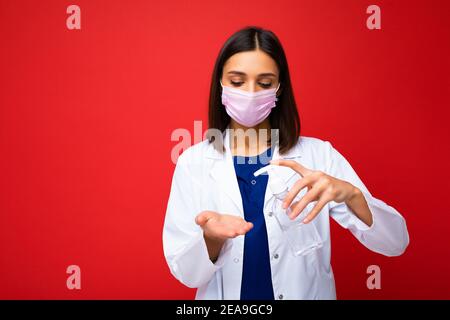 Consigli medici e protezione della salute durante l'epidemia di coronavirus. Giovane donna dottore in maschera protettiva, cappotto bianco mostra antisettico nelle sue mani Foto Stock