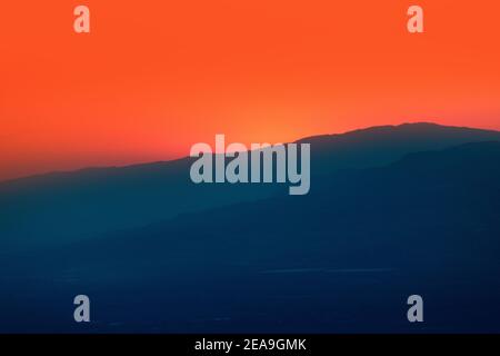 Il sole si trova dietro la grande montagna silhoutte Foto Stock