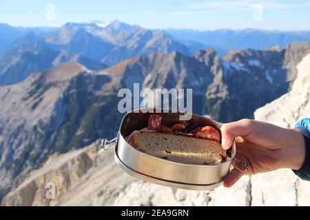 Escursione al Pleisenspitze (2569 m), la mano della donna tiene un pranzo al sacco con pane e salsiccia, tour in montagna, escursioni in montagna, all'aperto, sullo sfondo si può vedere il Brunstein, Wetterstein fino alle Zugspitze Foto Stock