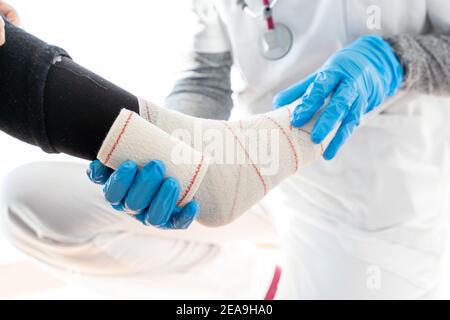 Crop medic in guanti di lattice che avvolgono la gamba di senior irriconoscibile paziente durante l'uso del bendaggio Foto Stock