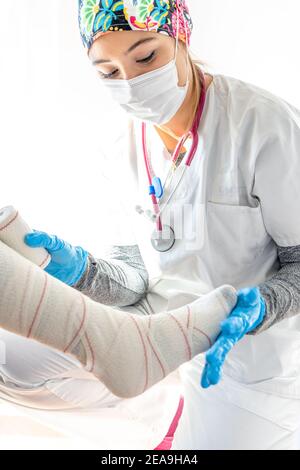 Crop medic in guanti di lattice che avvolgono la gamba di senior irriconoscibile paziente durante l'uso del bendaggio Foto Stock