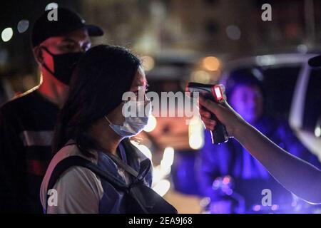 Un poliziotto controlla la temperatura corporea e l’identificazione delle persone in un checkpoint dopo essere stato dispiegato come parte della misura preventiva del governo contro la diffusione del coronavirus nel Metropolita Manila, Filippine. Foto Stock