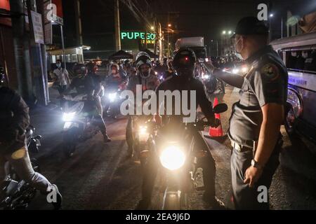 Un poliziotto controlla la temperatura corporea e l’identificazione delle persone in un checkpoint dopo essere stato dispiegato come parte della misura preventiva del governo contro la diffusione del coronavirus nel Metropolita Manila, Filippine. Foto Stock