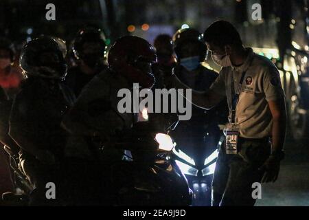 Un poliziotto controlla la temperatura corporea e l’identificazione delle persone in un checkpoint dopo essere stato dispiegato come parte della misura preventiva del governo contro la diffusione del coronavirus nel Metropolita Manila, Filippine. Foto Stock