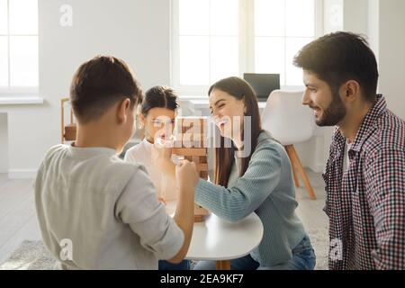 Felice giovane famiglia gioca con i loro figli e a turno rimuovere mattoni da una torre di legno. Foto Stock