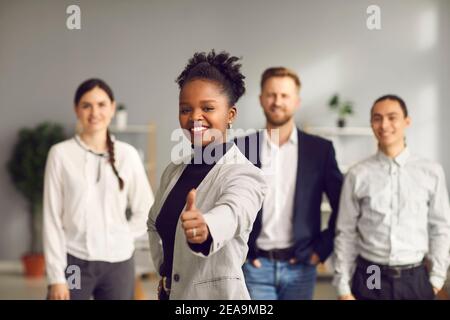 Donna nera che dà i pollici-in su e sorridente insieme con il gruppo di persone in background Foto Stock