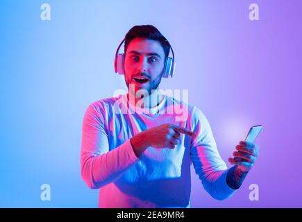 Un ragazzo millenario emozionato con un look a bocca aperta in cuffia alla telecamera Foto Stock