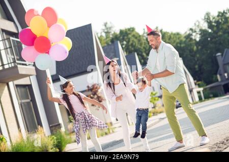 Ritratto fotografico della grande famiglia che indossa coni di compleanno mentre padre solleva il ragazzo all'aperto in estate sulla strada Foto Stock